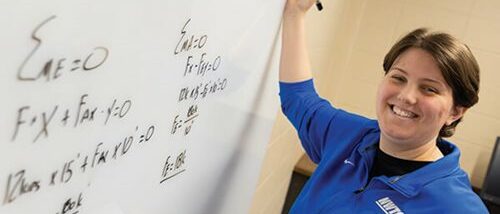 girl smiling at camera doing a math problem on white board